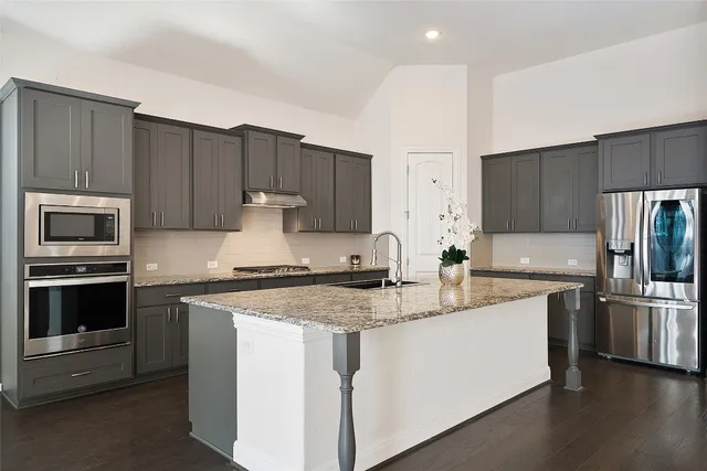 a kitchen with stainless steel appliances granite countertop a stove a sink and a refrigerator with wooden floor