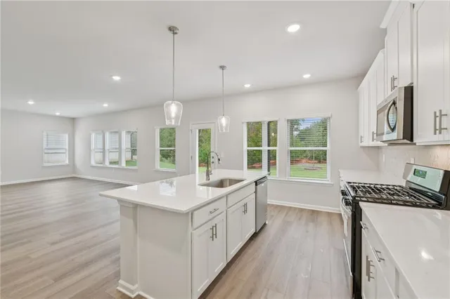 a kitchen with stainless steel appliances granite countertop a stove a sink and white cabinets with wooden floors