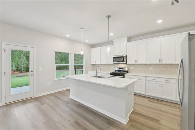 a large white kitchen with a sink a refrigerator and a stove top oven with wooden floor