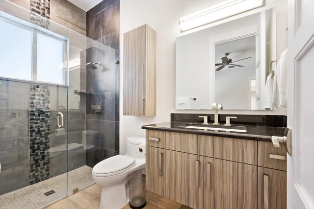 a bathroom with a granite countertop sink a toilet a mirror and shower