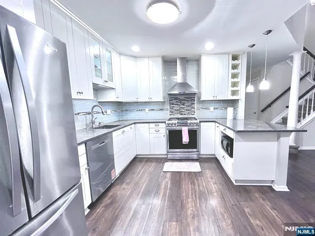 a large kitchen with stainless steel appliances granite countertop a stove a sink dishwasher a refrigerator white cabinets and wooden floor