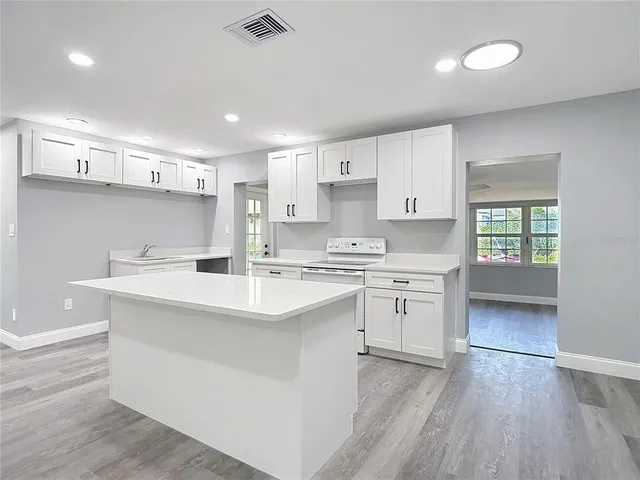 a kitchen with a white island cabinets and wooden floor