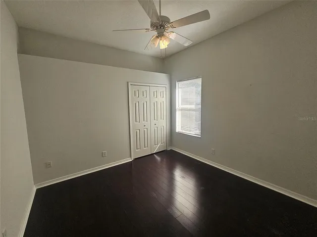 an empty room with wooden floor fan and windows
