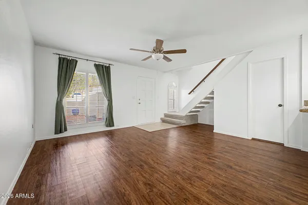 a view of an empty room with wooden floor ceiling fan and windows