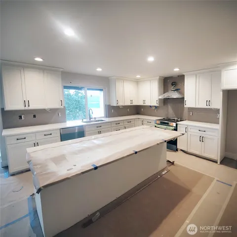 a large kitchen with kitchen island a sink a stove a refrigerator and a dining table with wooden floor