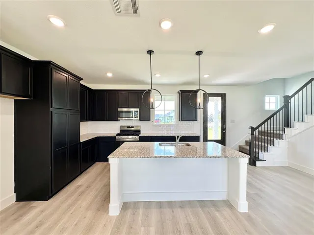 a large kitchen with stainless steel appliances kitchen island granite countertop a refrigerator a stove and a wooden floor