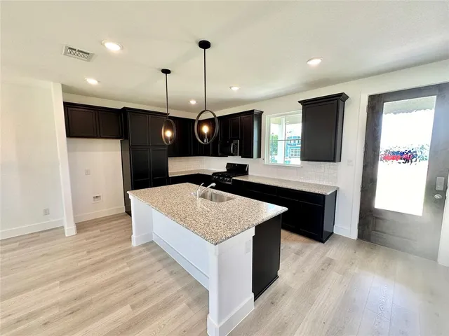 a large kitchen with stainless steel appliances kitchen island a chandelier and a wooden floor