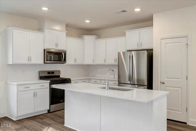 a kitchen with stainless steel appliances granite countertop a refrigerator stove a sink and white cabinets