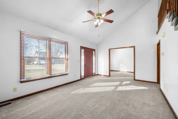 an empty room with chandelier fan and windows