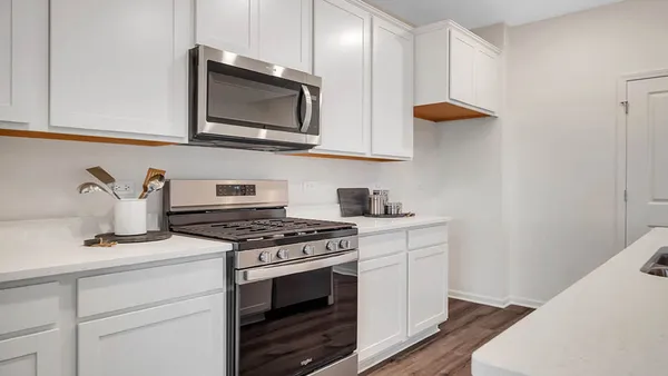 a kitchen with stainless steel appliances granite countertop a stove a sink a microwave a refrigerator and white cabinets with wooden floor