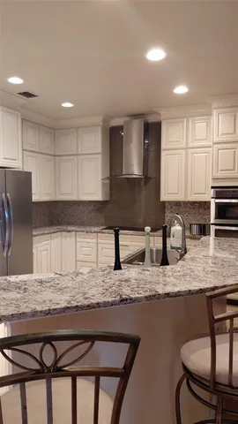 a kitchen with kitchen island granite countertop a stove a sink a refrigerator white cabinets and chairs