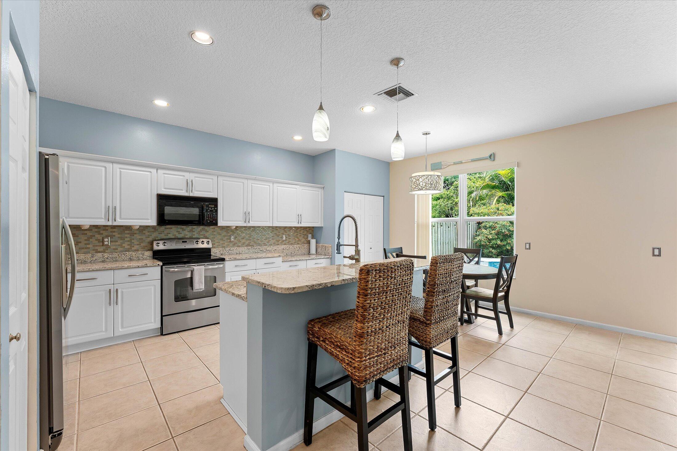 7061 Chesapeake Circle Boynton Beach, FL 33436 - Photo 9 of 51 a kitchen with kitchen island granite countertop stainless steel appliances a stove a sink a microwave a dining table and chairs