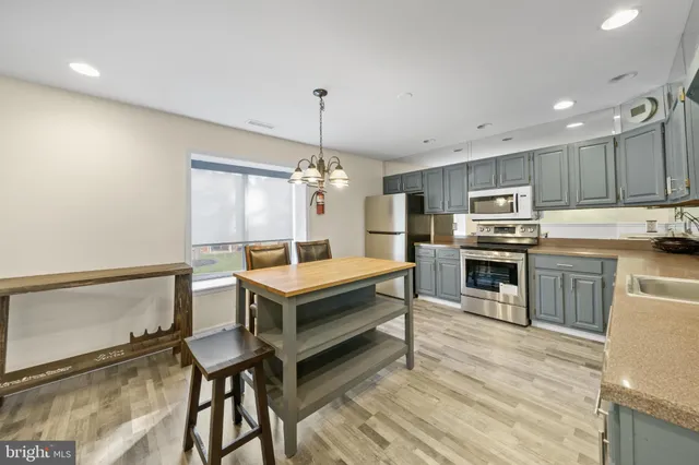 a open kitchen with stainless steel appliances granite countertop a stove top oven a sink dishwasher a dining table and chairs with wooden floor