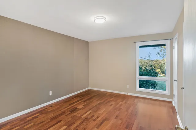 a view of an empty room with a window and wooden floor