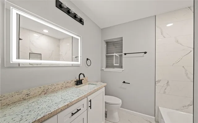 a bathroom with a granite countertop sink a toilet and a mirror