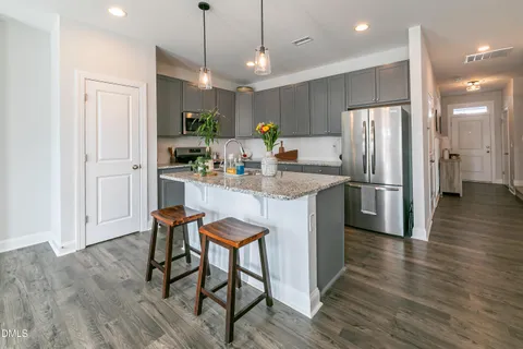 a kitchen with stainless steel appliances a dining table chairs refrigerator and sink