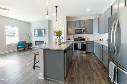 a kitchen with stainless steel appliances granite countertop a refrigerator a stove top oven a sink dishwasher and white cabinets with wooden floor