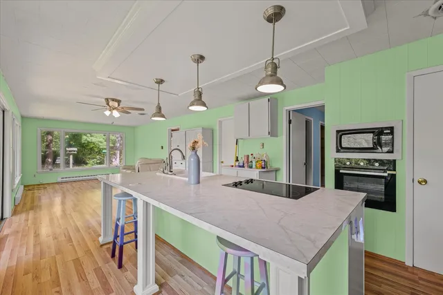 a open kitchen with stainless steel appliances granite countertop a refrigerator a microwave oven a sink dishwasher and a dining table with wooden floor