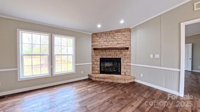 an empty room with wooden floor fireplace and windows