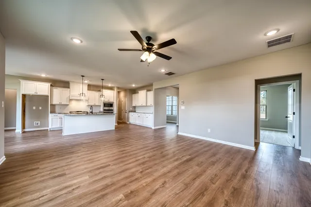 a view of an empty room and kitchen with wooden floor and a ceiling fan