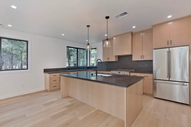 a kitchen with stainless steel appliances granite countertop a sink a stove a refrigerator and island with wooden floor