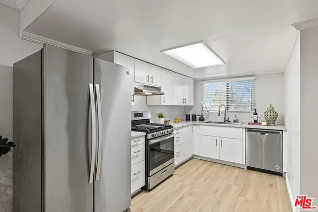 a kitchen with stainless steel appliances granite countertop a refrigerator a stove a sink and white cabinets with wooden floor