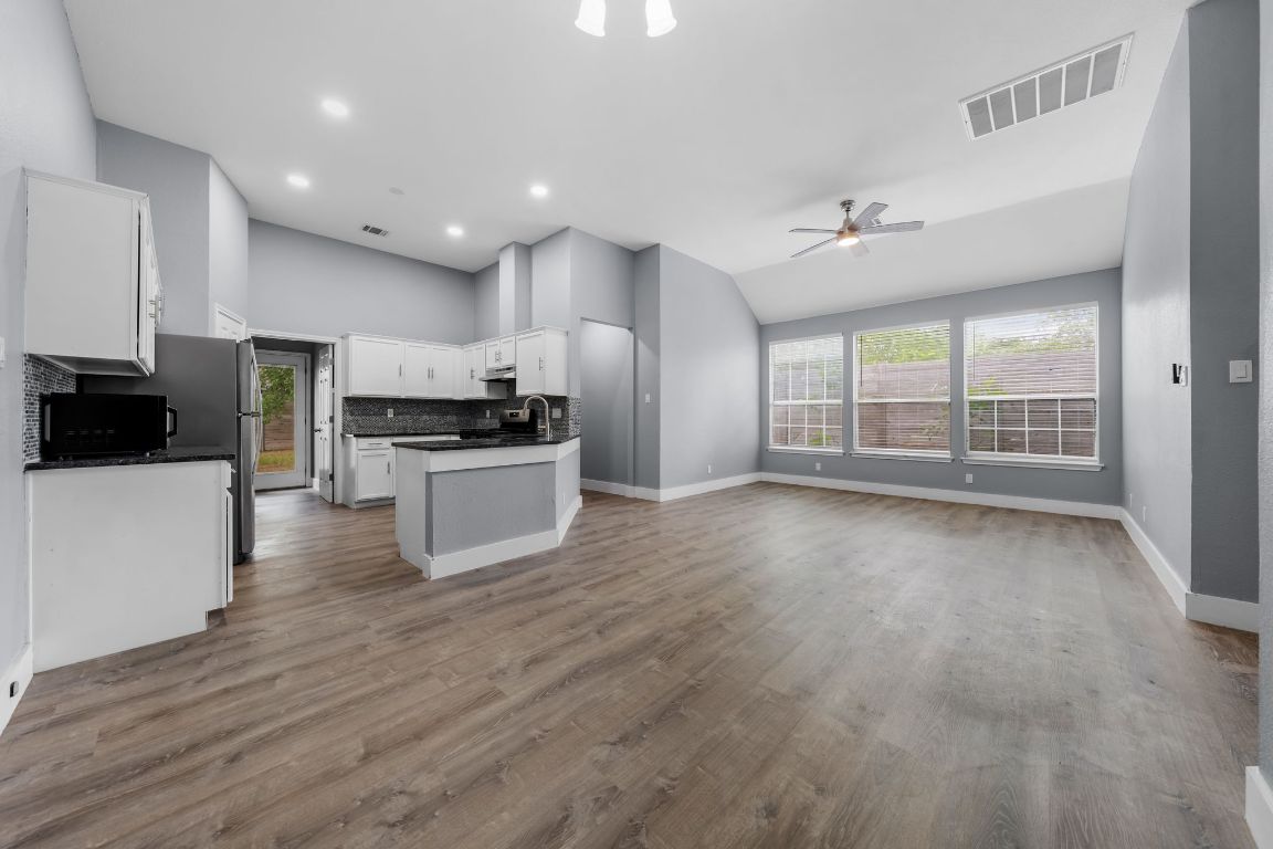 1214 Vargas Road, Unit A Austin, TX 78741 - Photo 25 of 25 Kitchen with open floor plan, tasteful backsplash, white cabinetry, vaulted ceiling, and black microwave