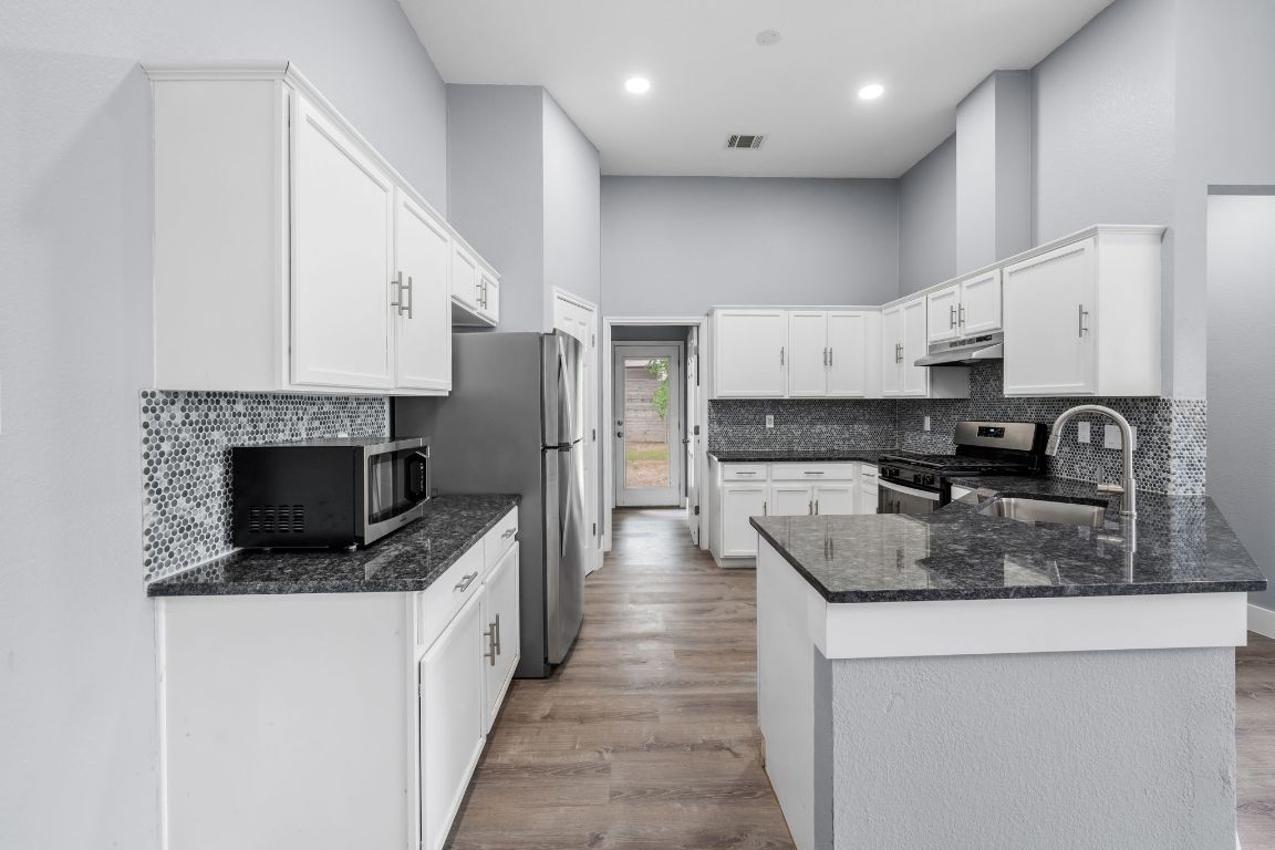 1214 Vargas Road, Unit A Austin, TX 78741 - Photo 9 of 25 Kitchen with white cabinets, dark stone countertops, decorative backsplash, light wood-type flooring, and a peninsula