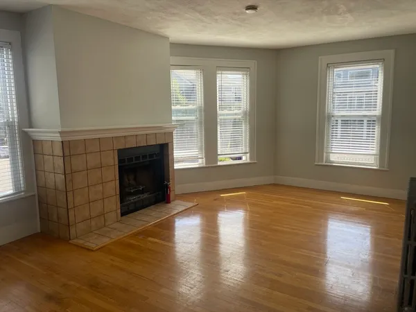 an empty room with wooden floor fireplace and windows