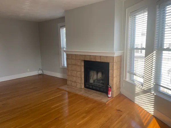 a view of an empty room with wooden floor fireplace and a window