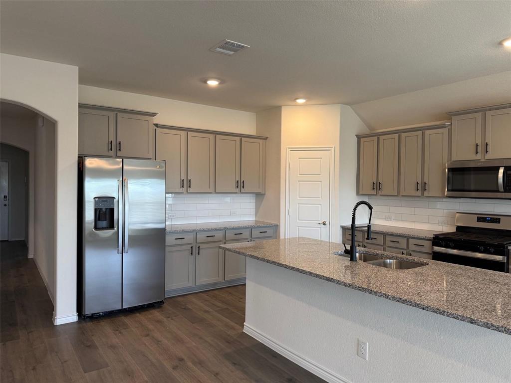 10314 Echo Brk Lane Aubrey, TX 76227 - Photo 2 of 21 Kitchen featuring appliances with stainless steel finishes, arched walkways, gray cabinetry, light stone counters, and dark wood-style floors