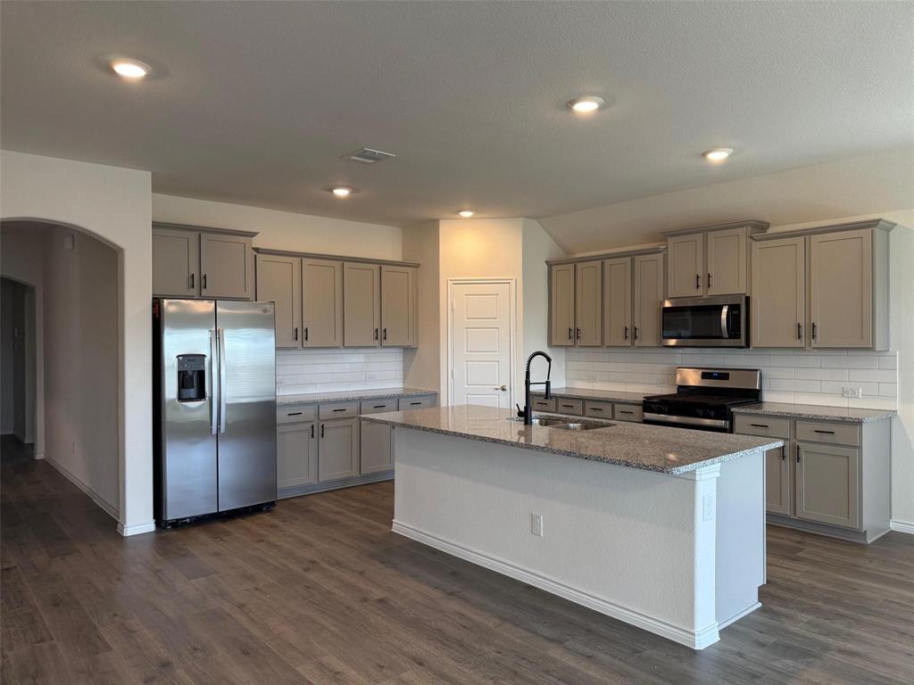 10314 Echo Brk Lane Aubrey, TX 76227 - Photo 3 of 21 Kitchen with tasteful backsplash, arched walkways, appliances with stainless steel finishes, light stone counters, and gray cabinetry