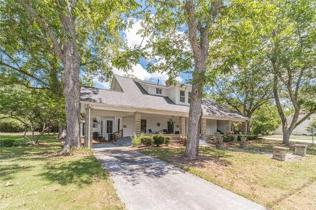 a view of a white house with a large tree and lawn chairs