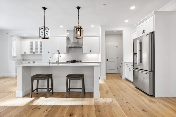 a kitchen with stainless steel appliances granite countertop a refrigerator a sink dishwasher a stove and white cabinets with wooden floor