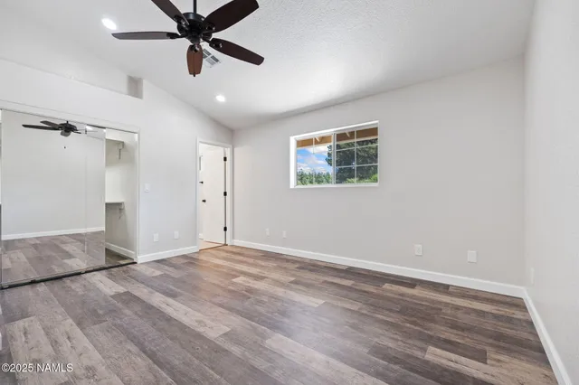 an empty room with wooden floor ceiling fan and windows