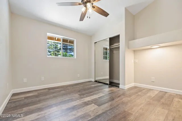 a view of an empty room with wooden floor and a ceiling fan