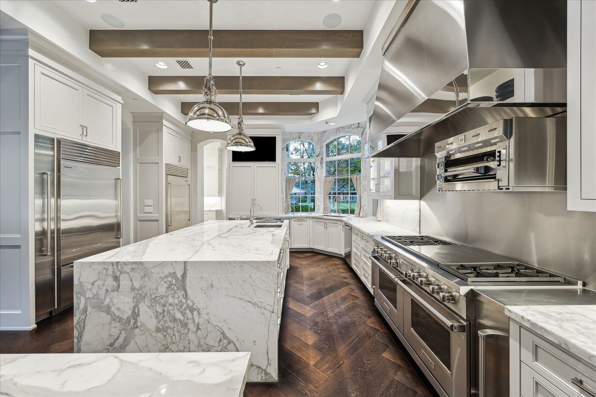 220 Merrie Way Lane Houston, TX 77024 - Photo 12 of 50 The marble waterfall island serves as the kitchen’s focal point, complemented by herringbone Wenge flooring, custom stained beams, sculptural pendant lighting, and a full-height marble backsplash that adds striking visual depth.