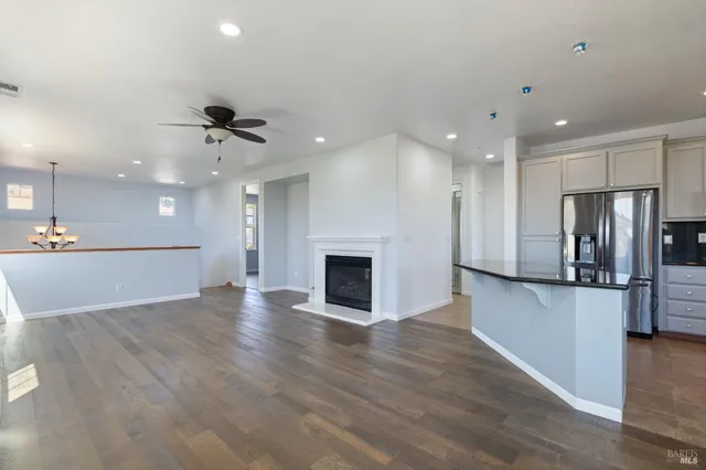 an empty room with wooden floor a kitchen view and a fireplace
