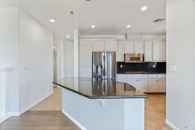 a kitchen with stainless steel appliances granite countertop a refrigerator a sink a stove a microwave and white cabinets