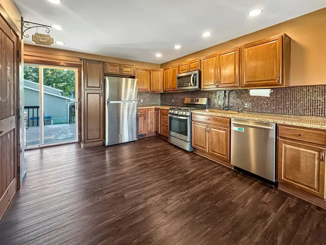 a kitchen with stainless steel appliances granite countertop a refrigerator a sink dishwasher a stove with wooden cabinets and floor