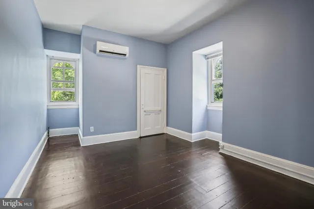 a view of an empty room with wooden floor and a kitchen