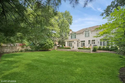 a view of a white house in front of a big yard with large trees