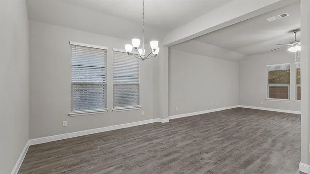 an empty room with wooden floor chandelier and windows