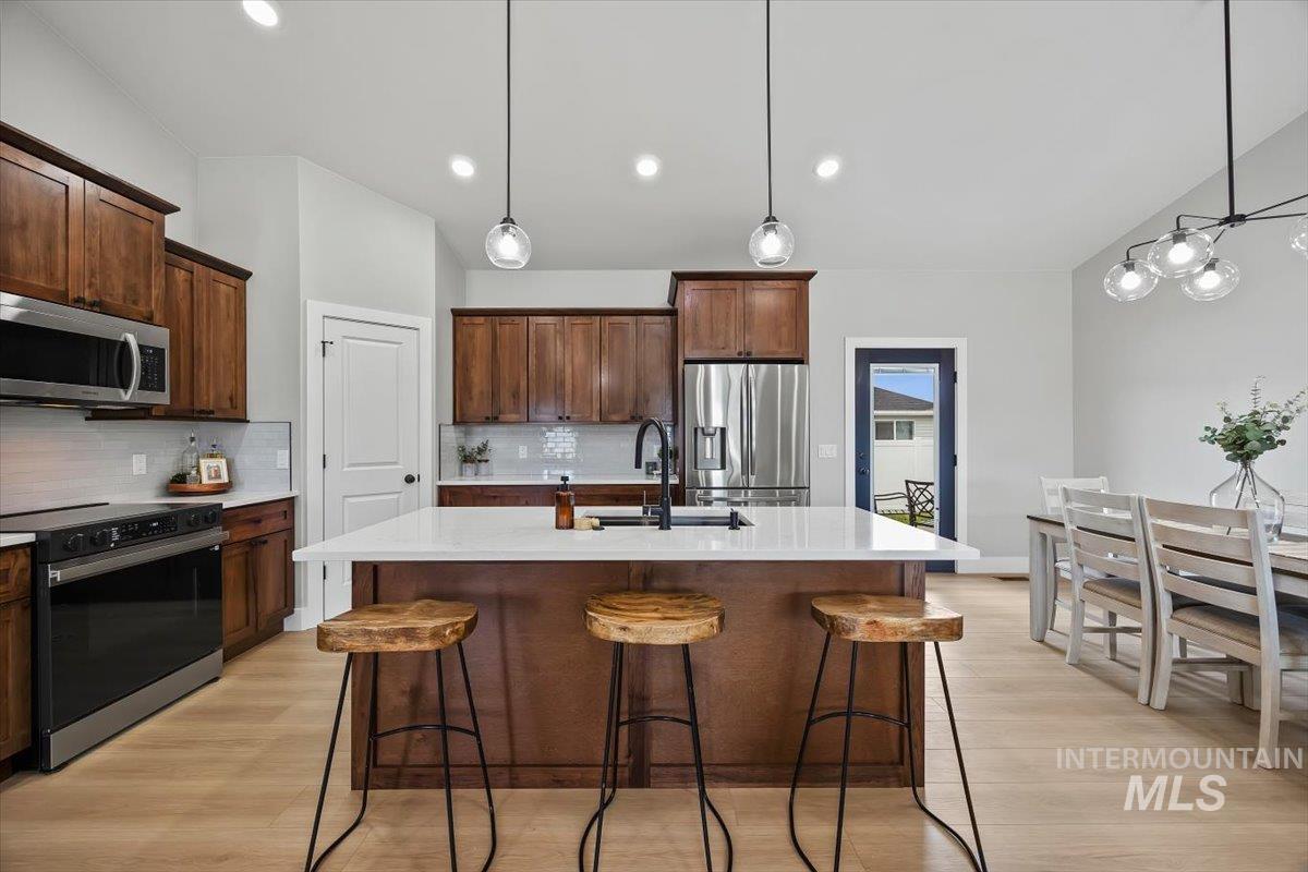 1201 Jade Drive Rupert, ID 83350 - Photo 8 of 27 Kitchen featuring a large island with a white countertop and seating, stainless steel appliances, wood-finish cabinetry, light wood-finish flooring, and pendant lighting