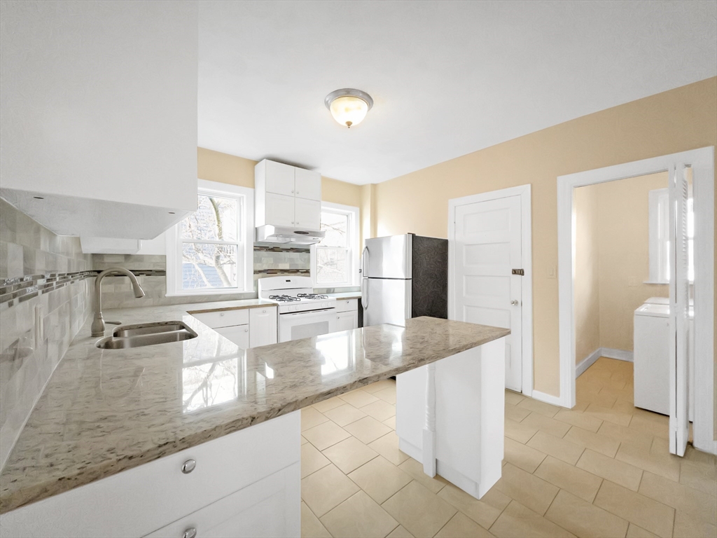 a view of a kitchen with kitchen island a counter top space a sink a refrigerator and cabinets