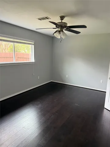 an empty room with wooden floor fan and windows