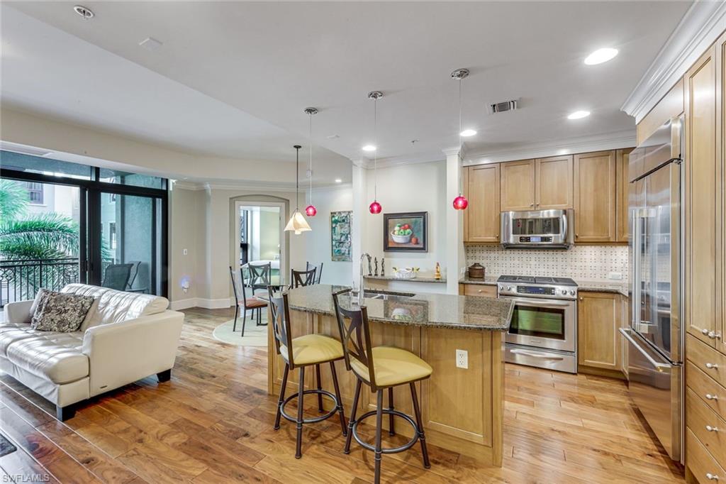 9123 Strada Place, Unit 7201 Naples, FL 34108 - Photo 6 of 50 a kitchen with stainless steel appliances granite countertop a stove top oven a sink dishwasher a dining table and chairs with wooden floor