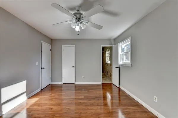 a view of an empty room with wooden floor and a ceiling fan