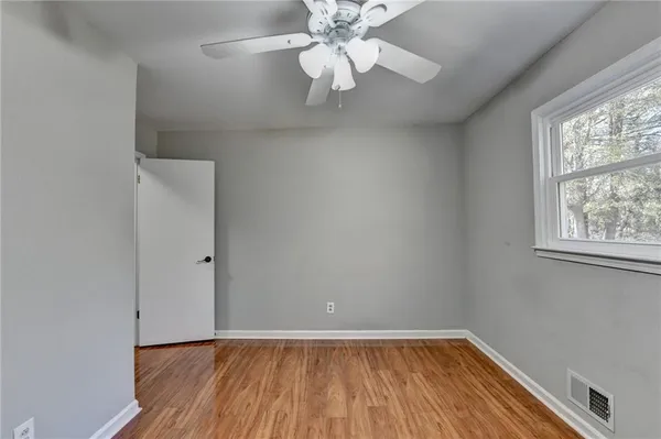an empty room with wooden floor fan and windows