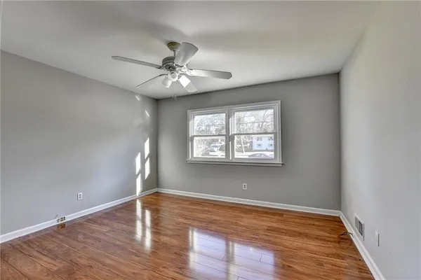 an empty room with wooden floor chandelier fan and windows